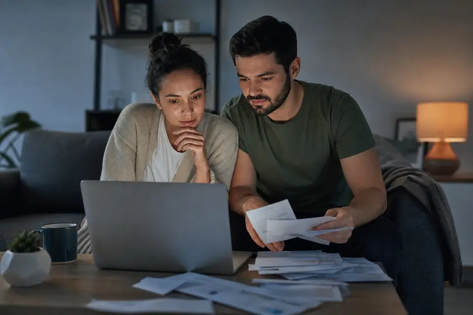 Young couple on a couch reviewing options on a laptop with opened mail