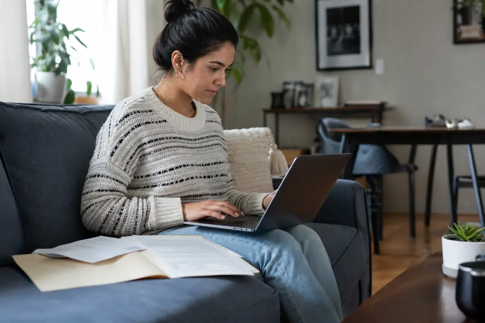 Woman on a couch verifying her identity online with a letter and tax folder