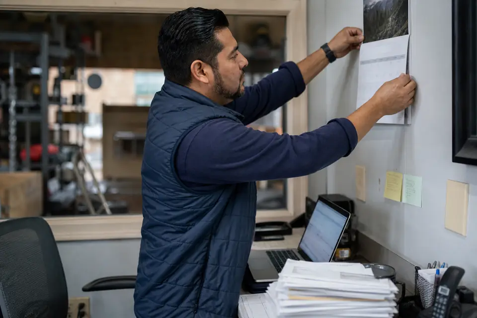 Small-business owner hanging a wall calendar above a desk in a back office